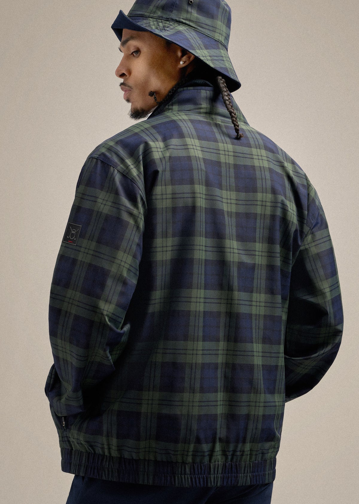 Black Male model wearing a plaid bucket hat and matching jacket, shown from the back while looking over his left shoulder, creating a stylish and dynamic pose.